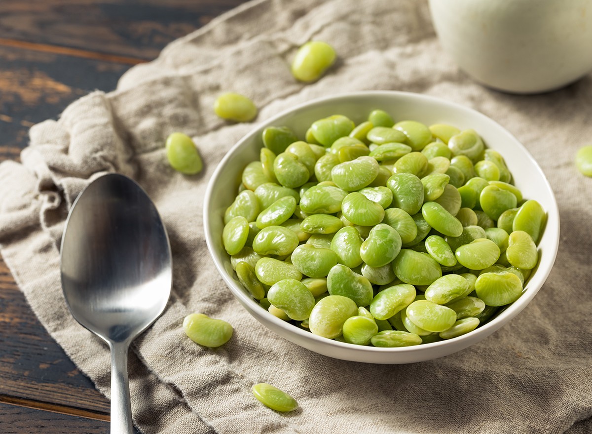 A bowl of lima beans and a spoon on a wooden table