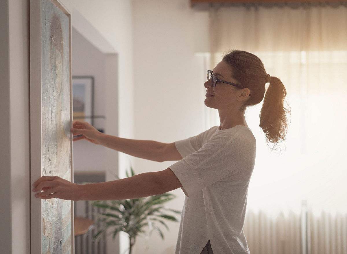 A woman hangs a canvas on a wall in room