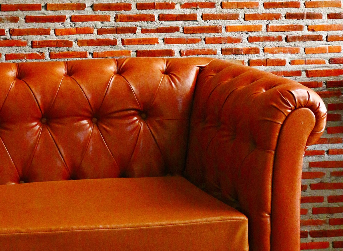 An upholstered leather sofa against a red brick wall