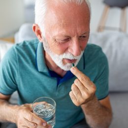 mature man in blue polo shirt taking a vitamin