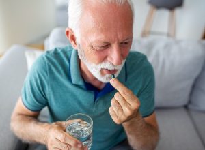 mature man in blue polo shirt taking a vitamin