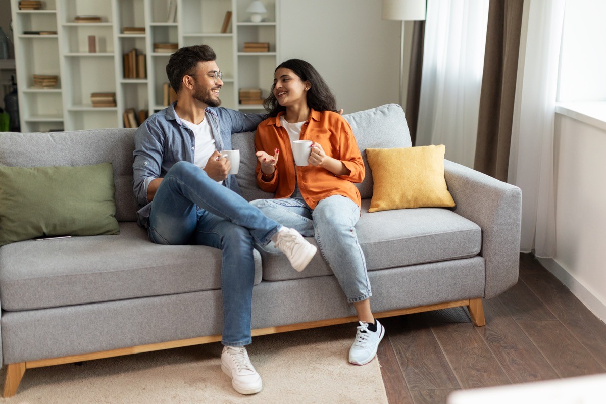 Happy couple relaxing and drinking coffee, sitting on couch at home