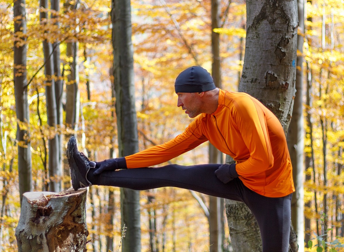 A man stretches his hamstrings while out walking in the woods
