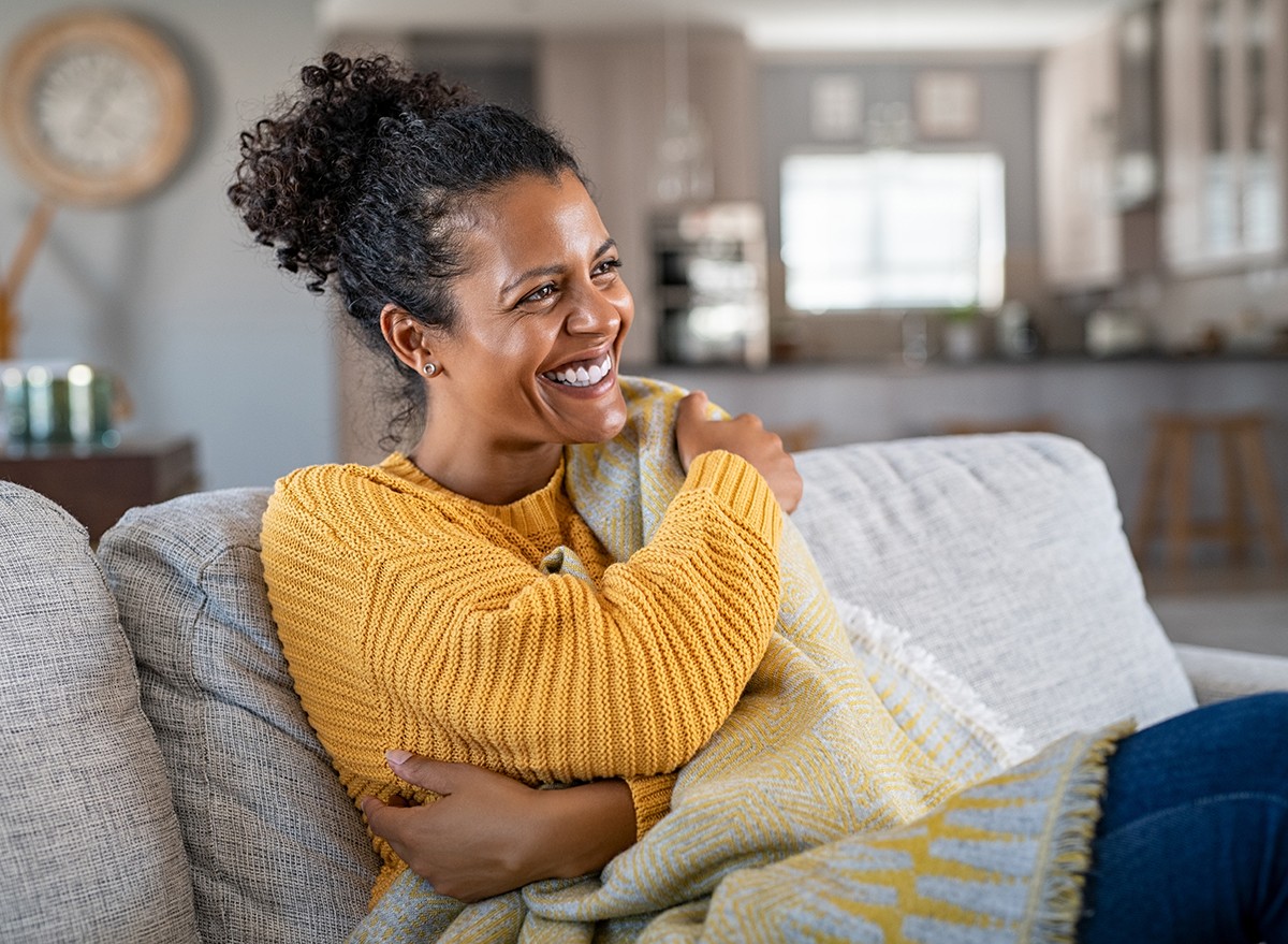 A woman sitting on the couch wrapped in a blanket to stay warm