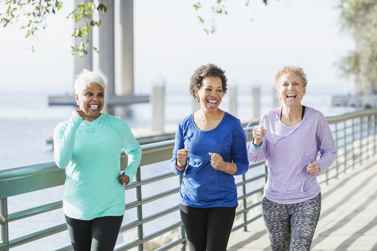 A group of three mature women power walking on a city waterfront side by side.