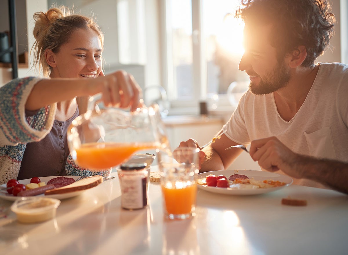 A couple eat breakfast together in the morning sunlight. 