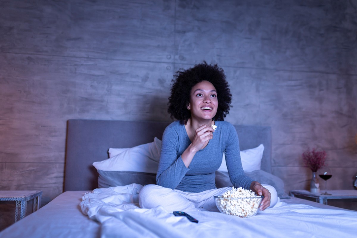 A woman eating popcorn in bed, staying up late