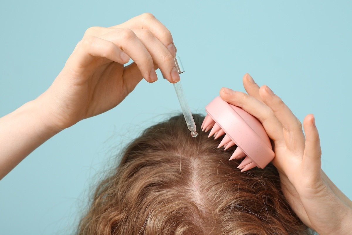 cropped image of the top of a woman's head while she applies a scalp oil and uses a scalp massager