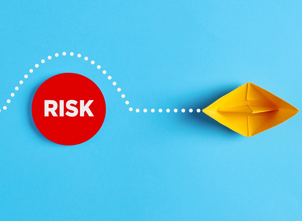 A paper boat sailing around a sign that says, 'RISK'