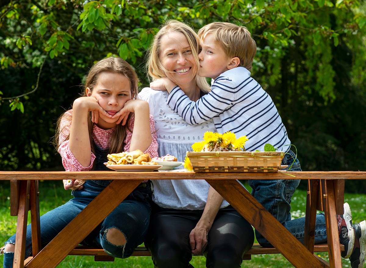 A mother at a picnic table with two children, one is jealous of the other