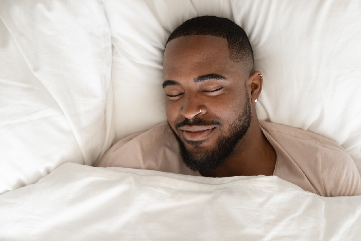 A  man sleeping in a comfortable white bed having a pleasant dream