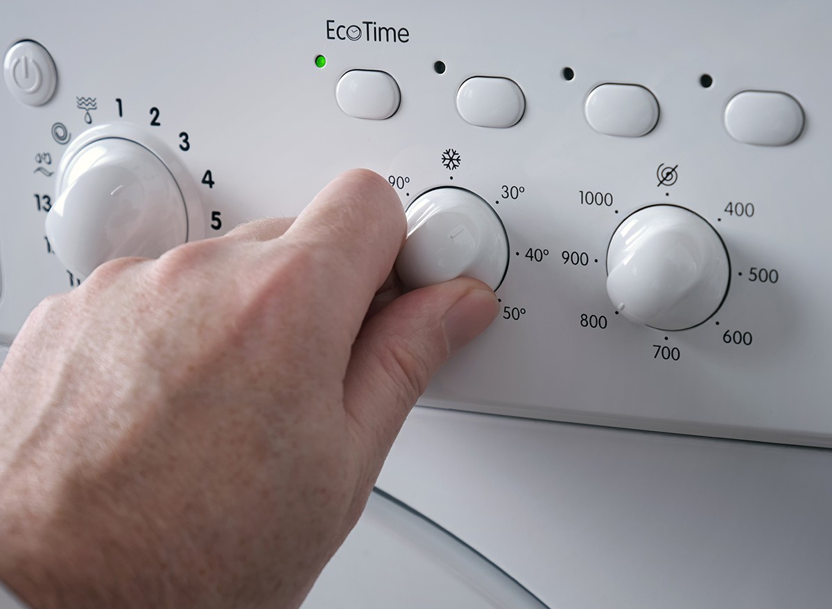 A man's hand adjusts the temperature on a washing machine before doing laundry