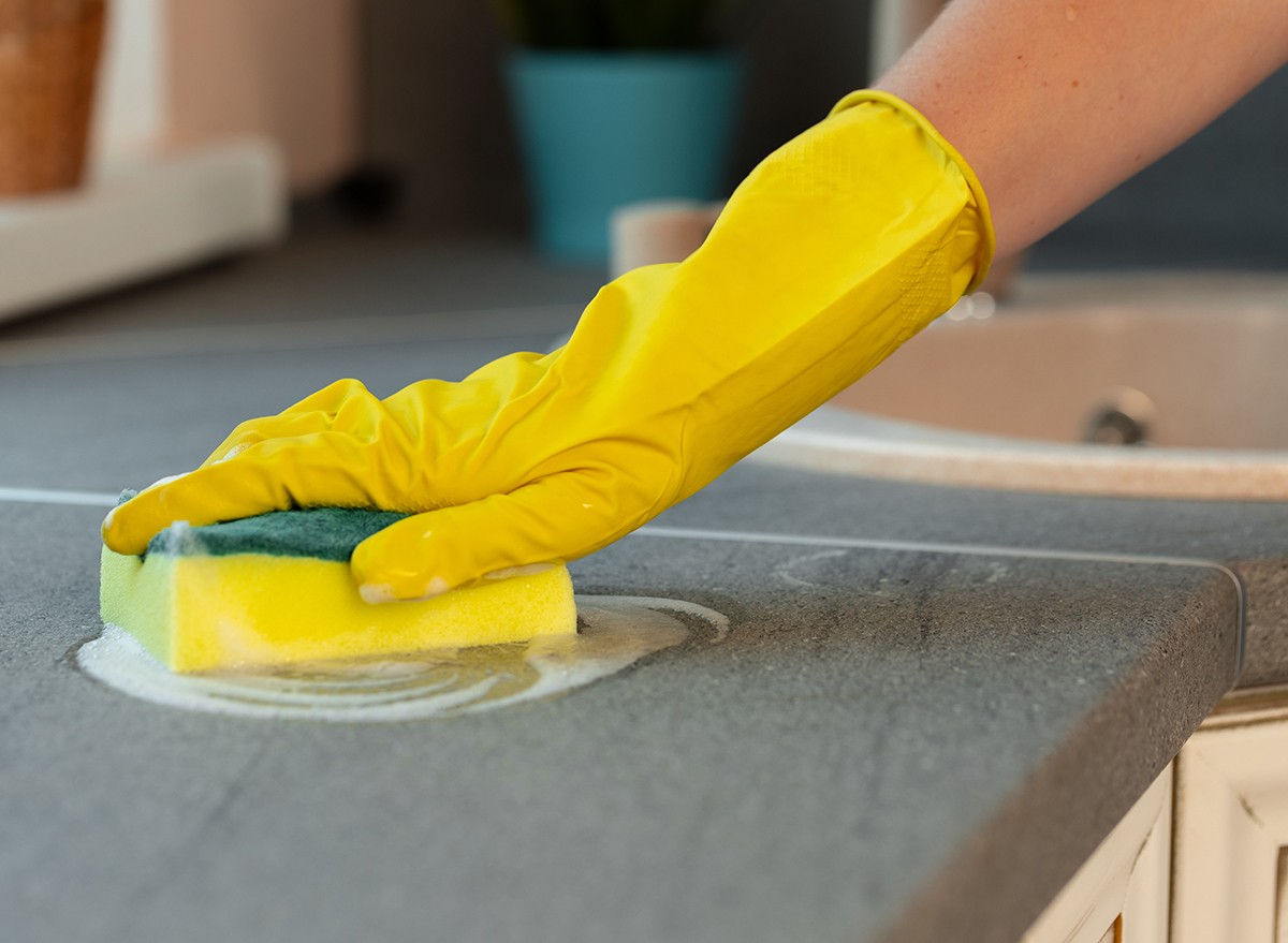 A gloved hand using a sponge to wipe a counter in the kitchen