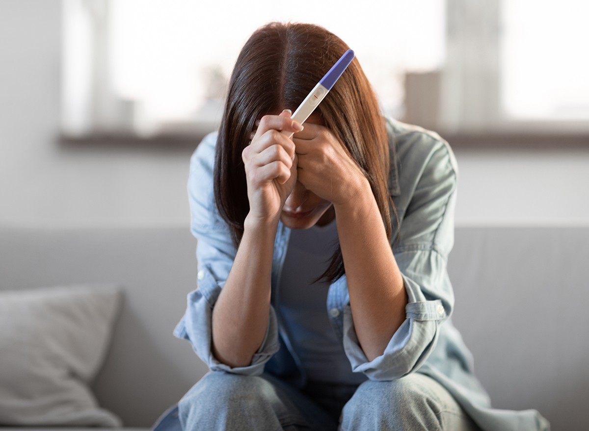 A woman holding a pregnancy test with her head in her hands
