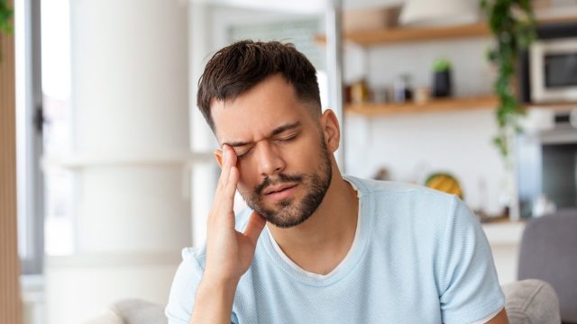 A man holding his head with his eyes closed suffering from a headache