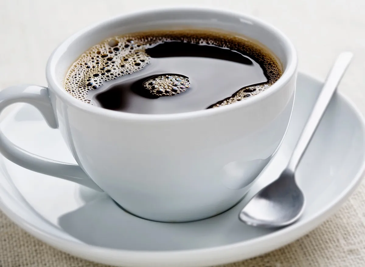A cup of black coffee in a white mug on a saucer with a spoon