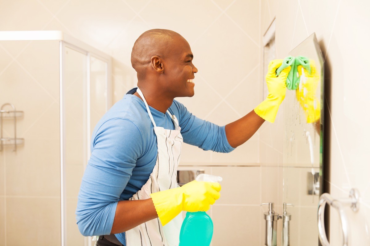 A young man cleaning bathroom mirror