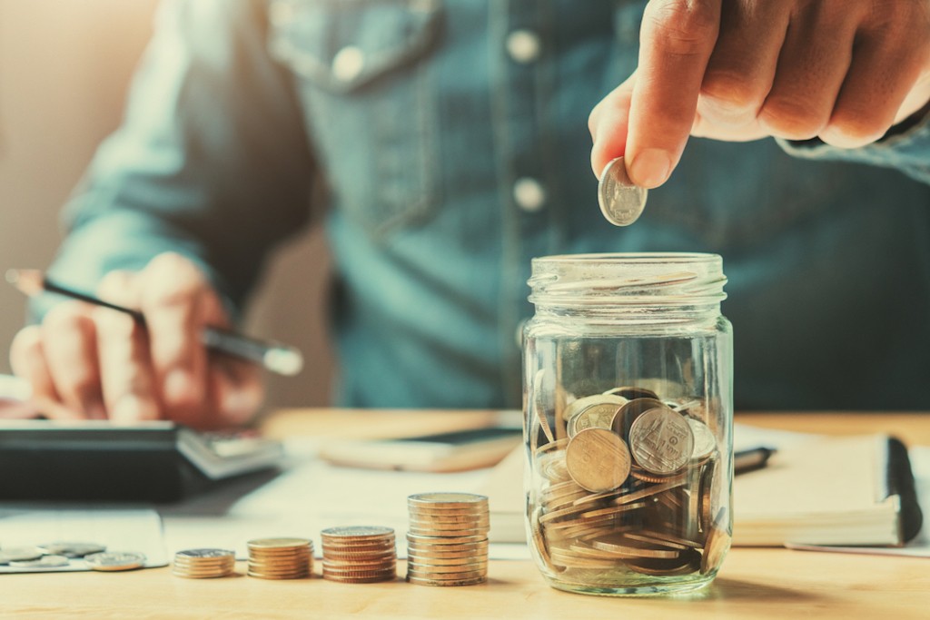A man putting coins in a jar for savings