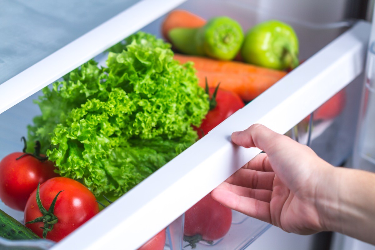 A woman's hand opening fridge with vegetables
