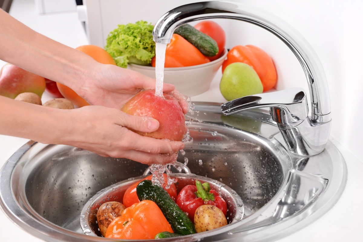 person washing fruits and vegetables in a metal kitchen sink