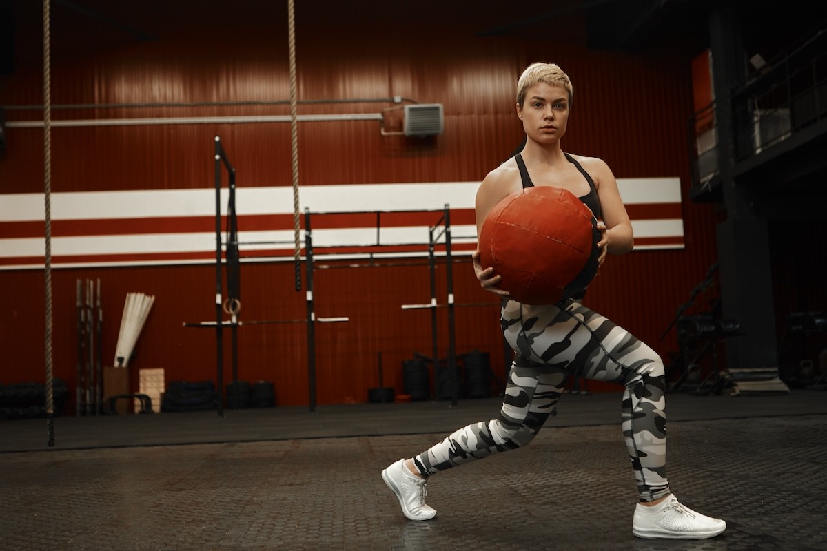 fit woman doing a twisting lunge with a weighted medicine ball in the gym