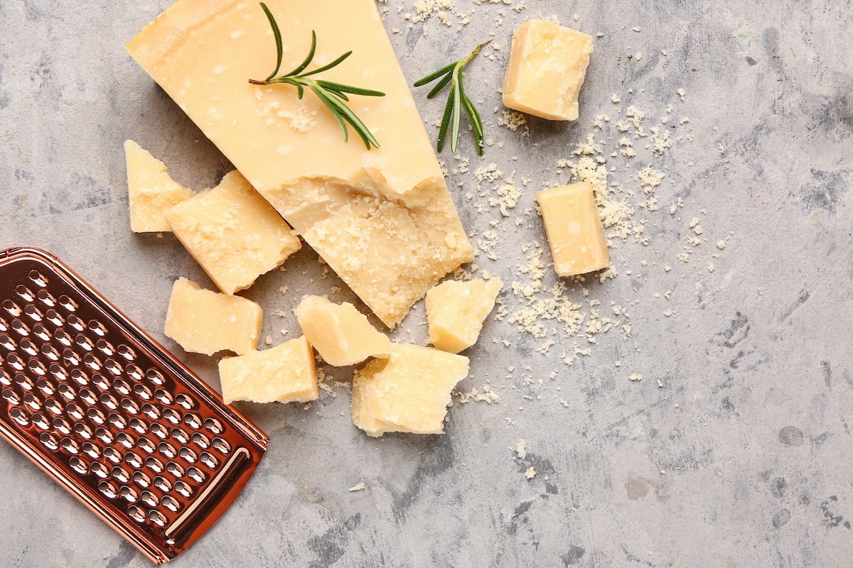 Parmesan chunks and a cheese grater on a gray surface