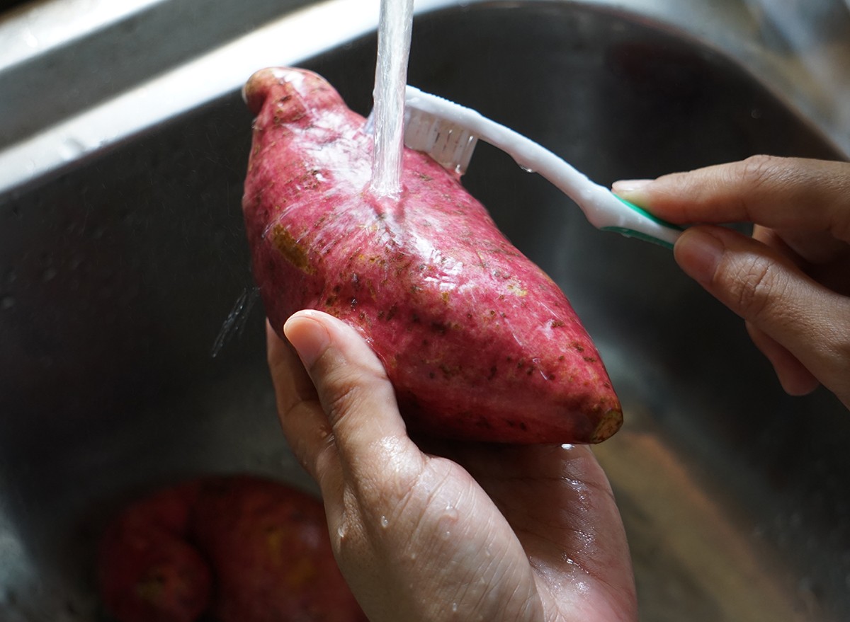 Hands washing a sweet potato with a cold water and a toothbrush