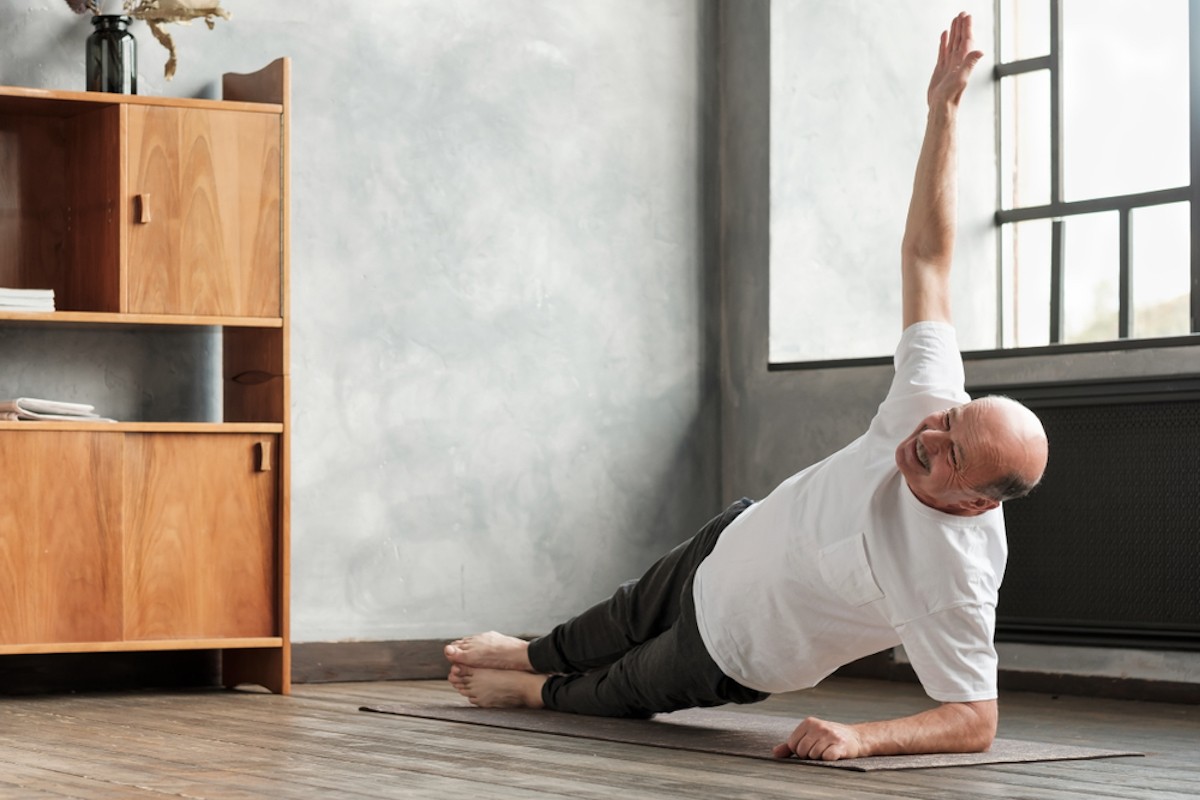 Senior man man doing a side plank exercise at living room