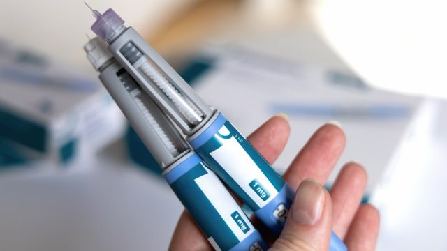 closeup of a hand holding two Ozempic pens