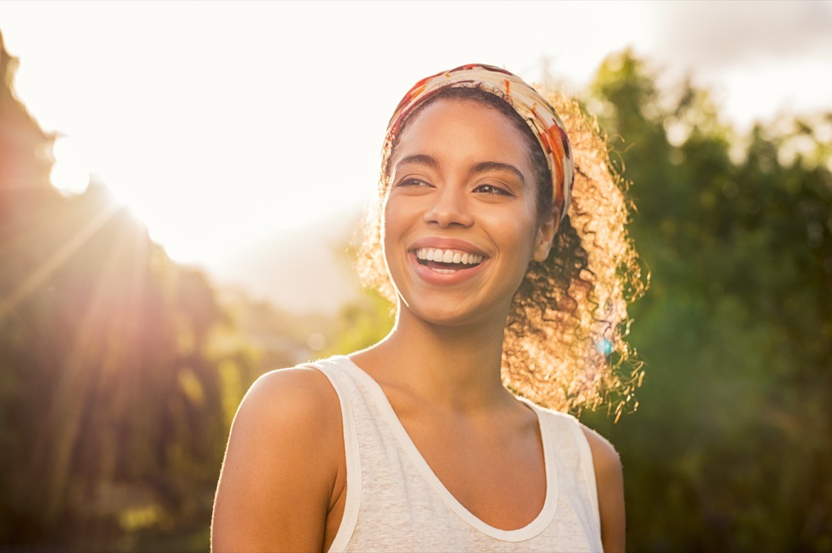 A woman smiling and looking away at park during sunset