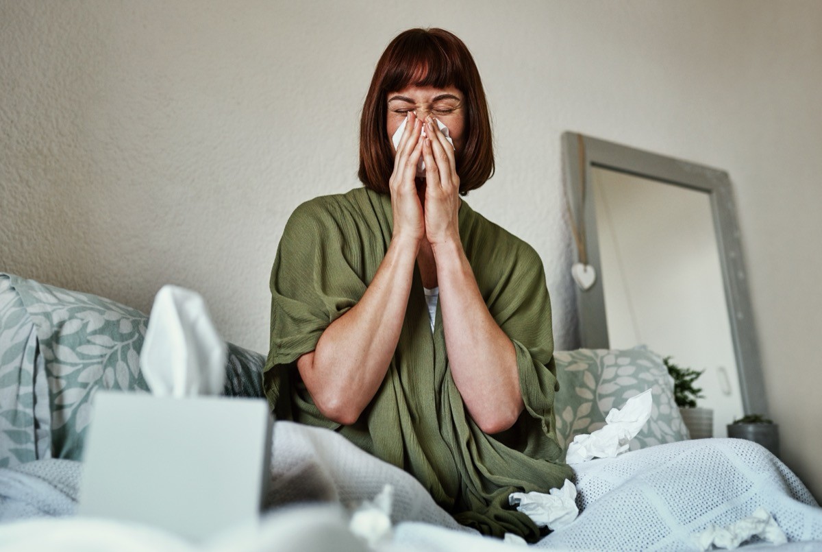 woman in bed suffering with a cold, blowing her nose