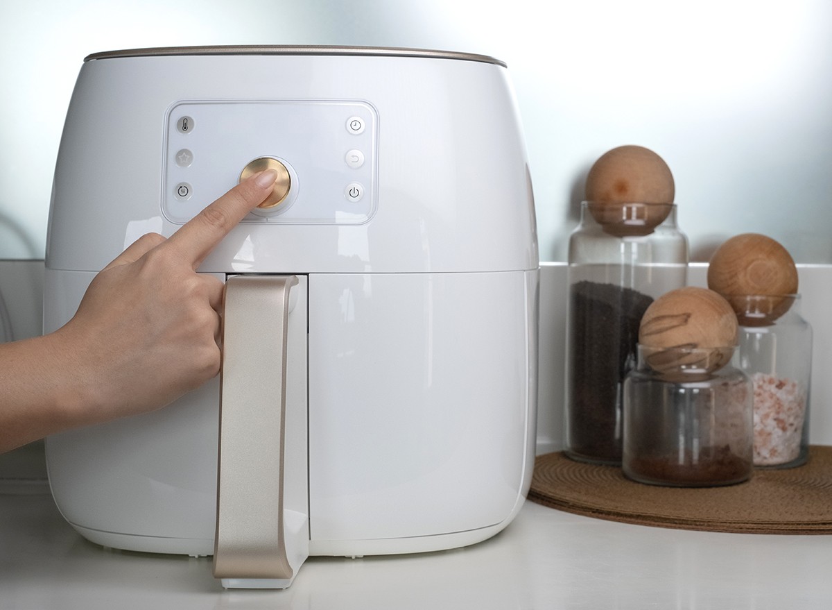 A woman's hand presses a button on an air fryer