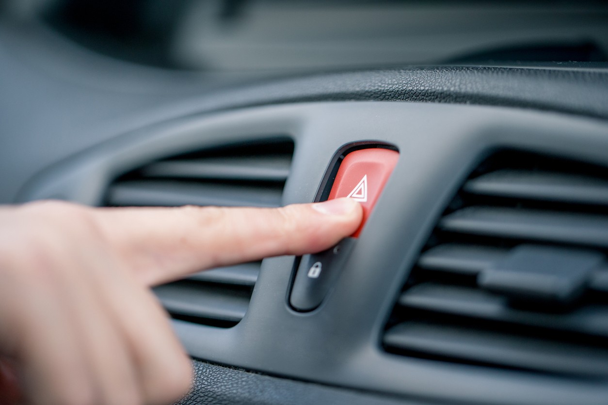 A person pressing the button to turn on the hazard lights in a car