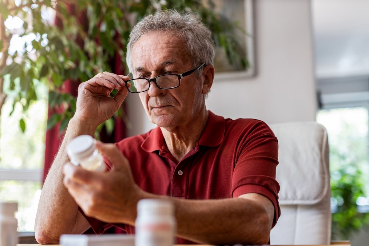 mature man in a red shirt reading a supplement or medication bottle
