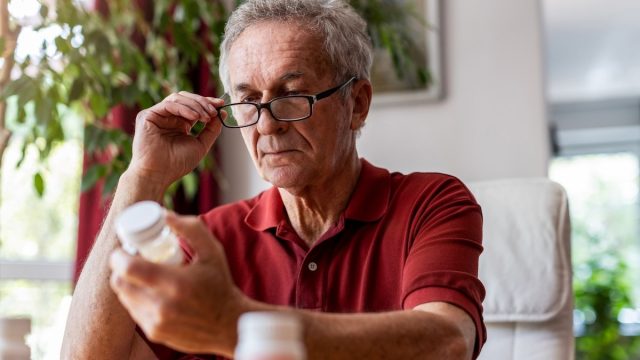 mature man in a red shirt reading a supplement or medication bottle