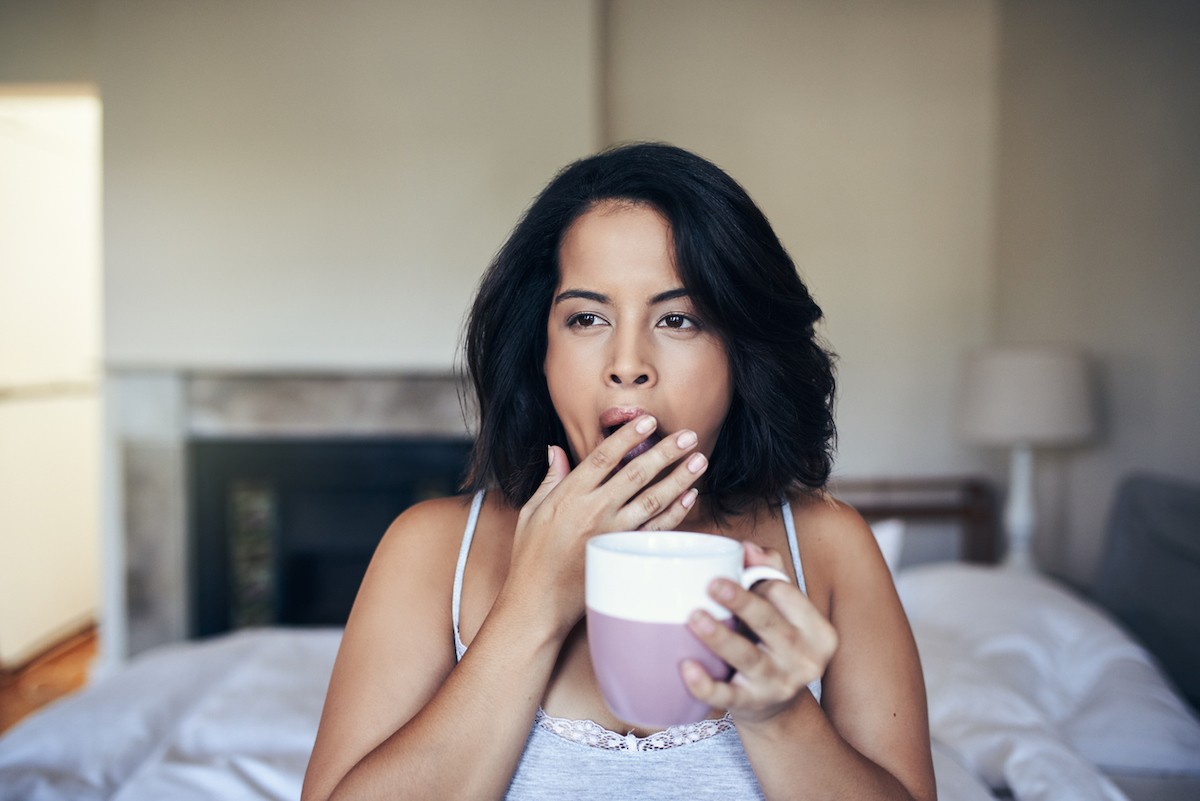 A woman yawning while having coffee in the morning at home