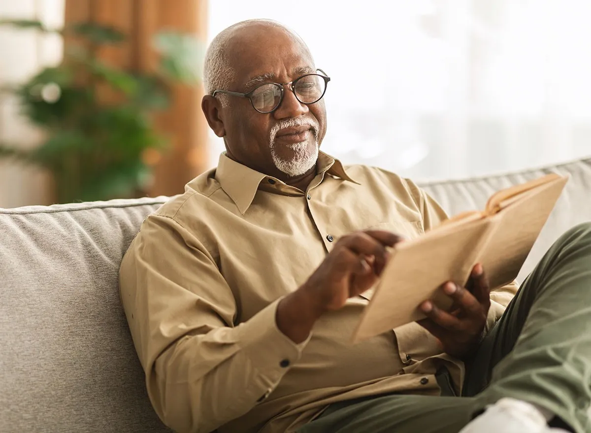 A senior man reading a book on the couch