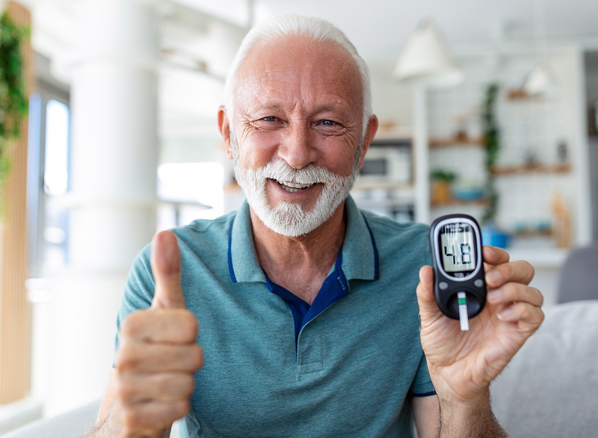 A smiling man holding a blood sugar meter and giving the thumbs up
