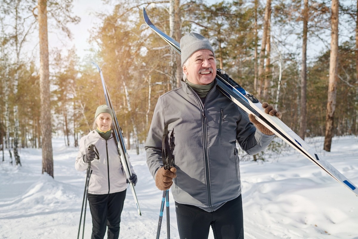 senior couple carrying skis and poles on snowy hill