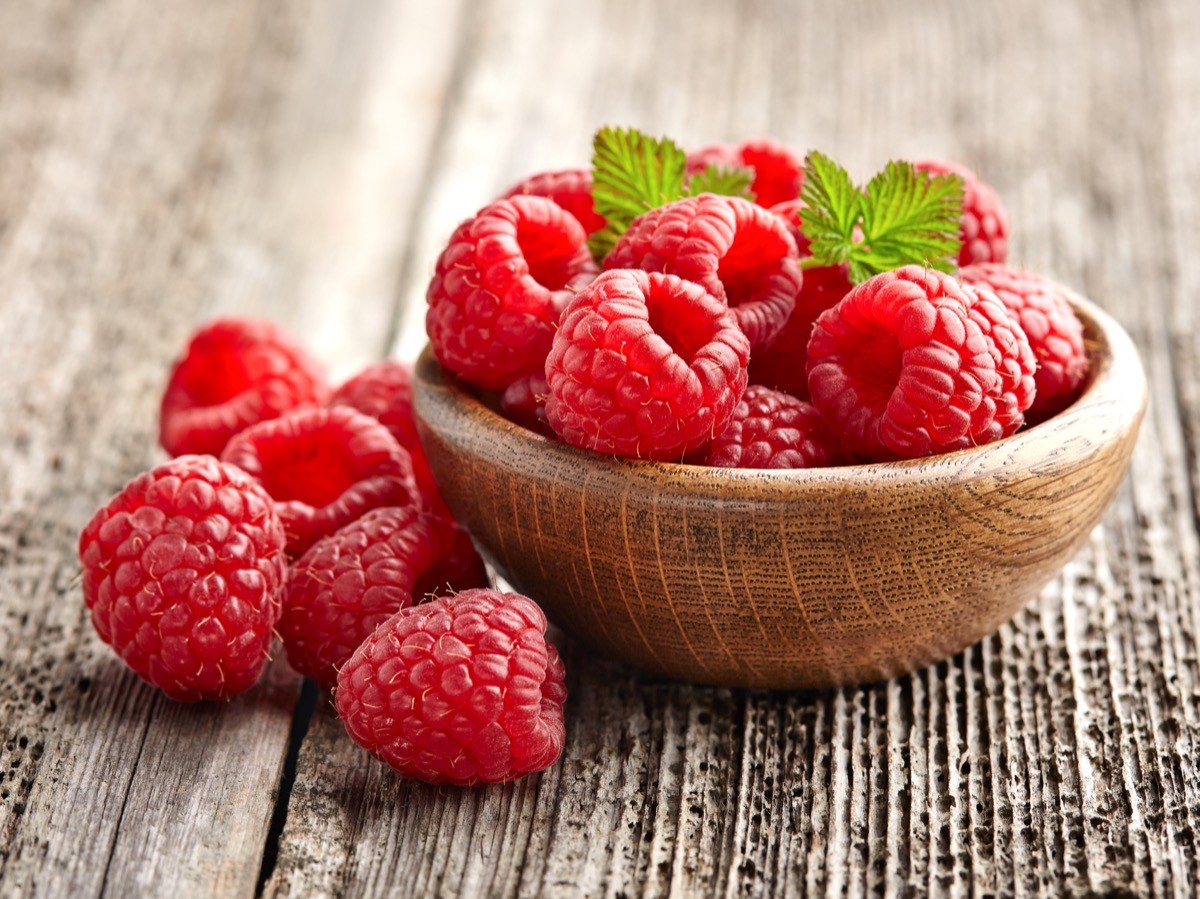 raspberries in a small wooden bowl on a wood table