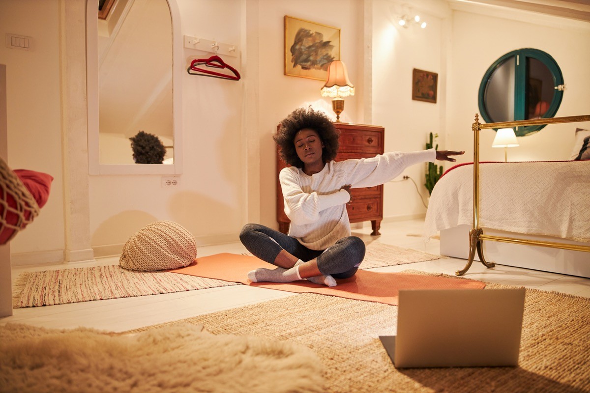 woman sitting on an exercise mat at home, doing yoga.
