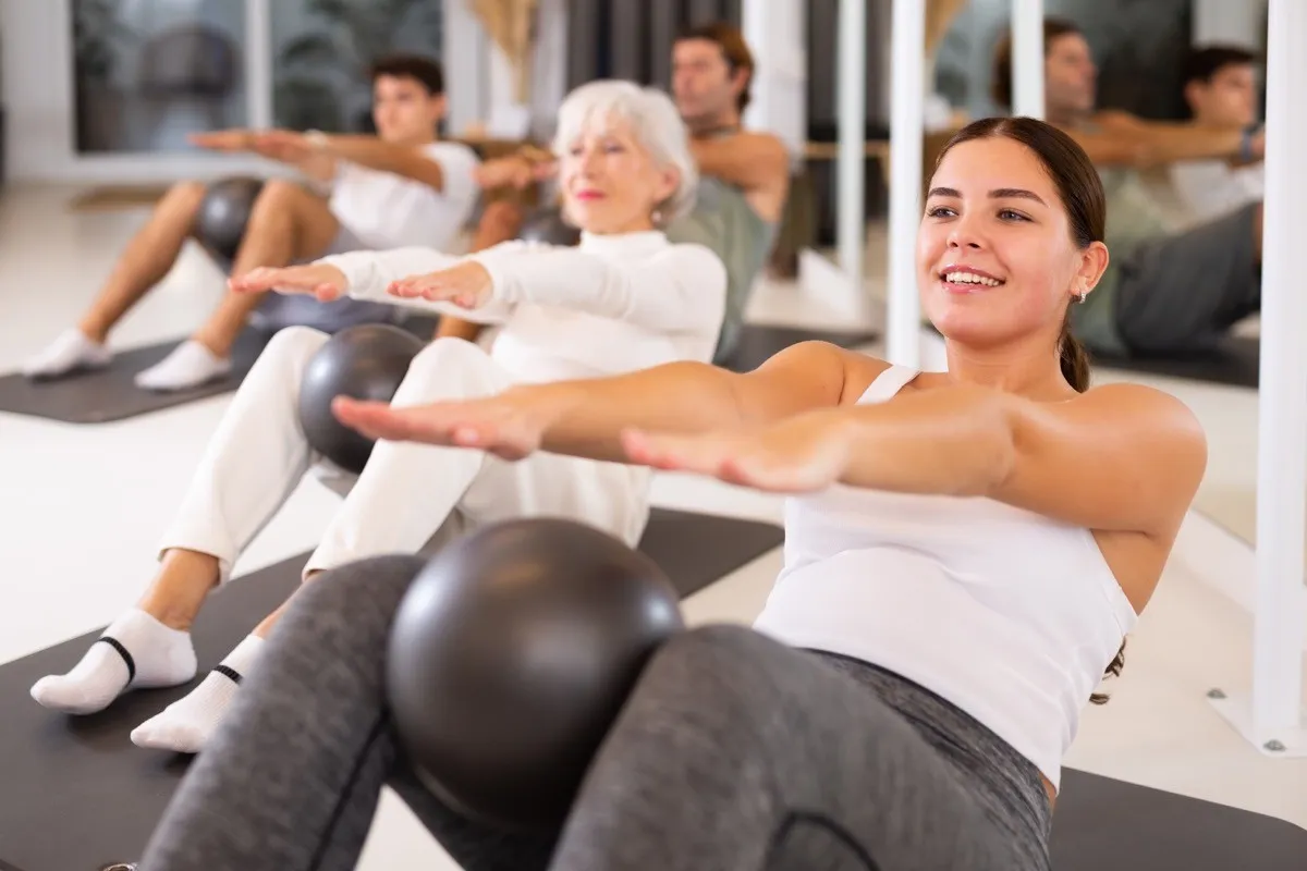 Adult people different ages practicing pilates with ball at group class in yoga studio