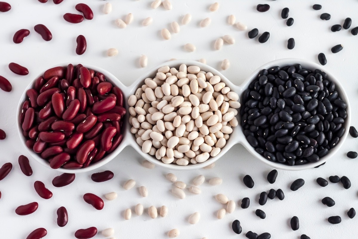 red kidney beans, white beans, and black beans in white bowls on a white surface