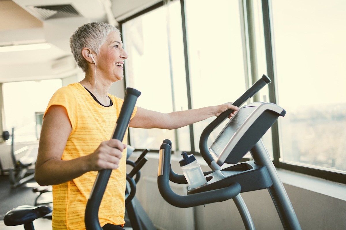 mature woman in a yellow t-shirt using the elliptical machine at the gym