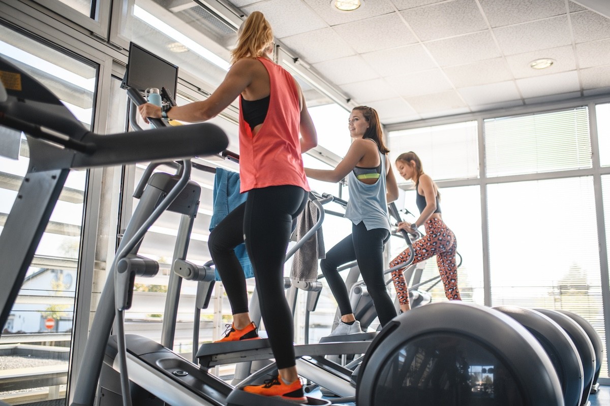 three young women using elliptical machines at the gym