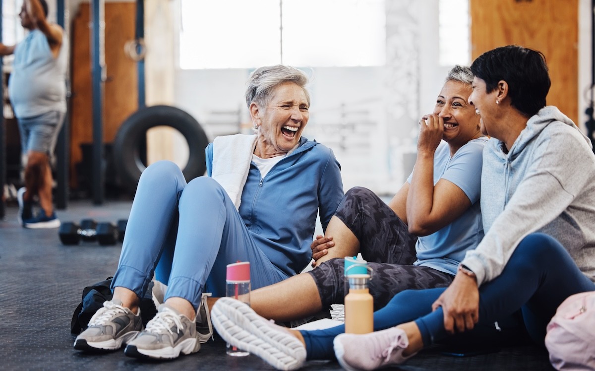 three mature women sitting on the floor at the gym, talking and laughing