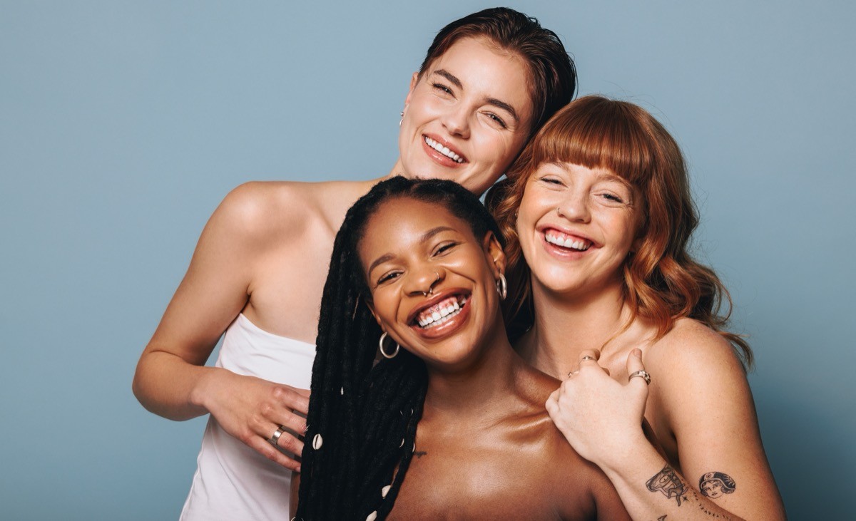 Cheerful women with different skin tones smiling at the camera in a studio.