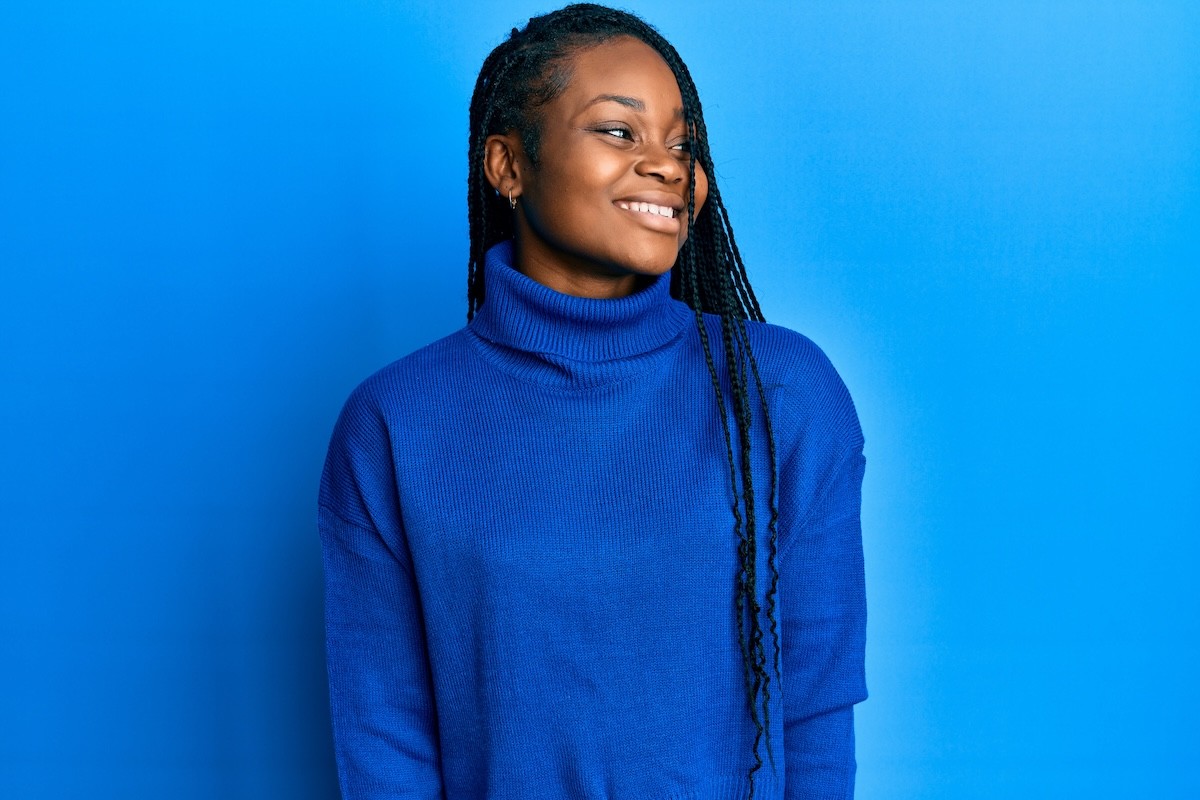 woman wearing a royal blue turtleneck sweater standing against a blue wall