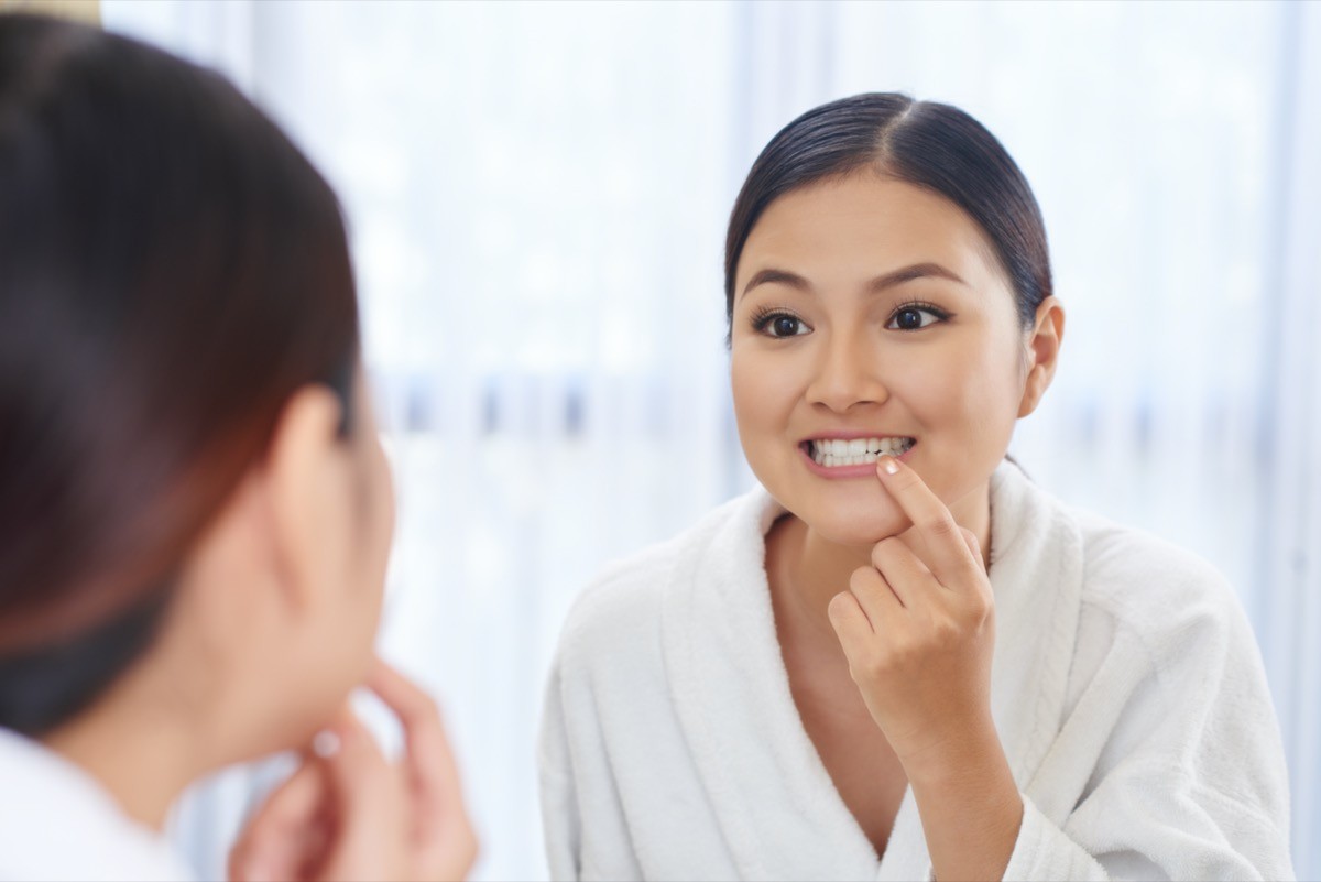 young woman looking at her teeth in the mirror