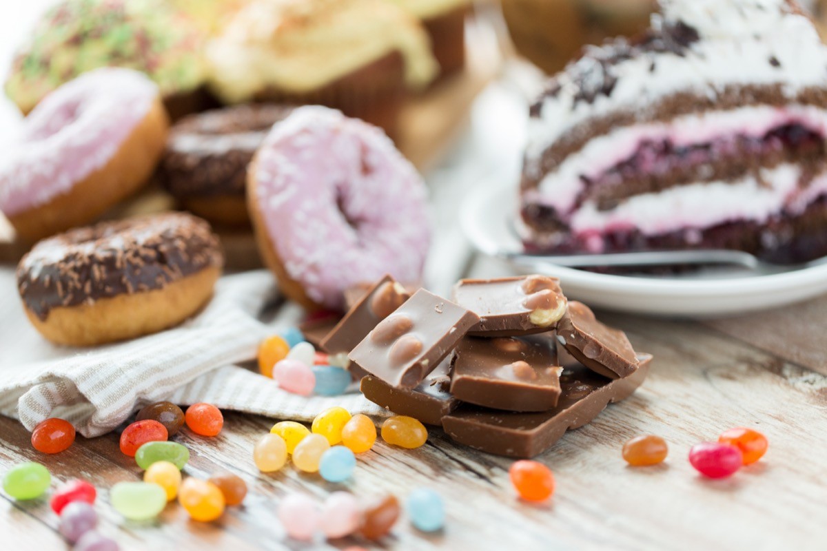 junk food, sweets and unhealthy eating concept - close up of chocolate pieces, jelly beans, glazed donuts and cake on wooden table